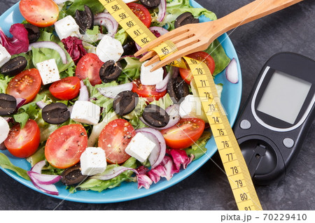 Glucometer, tape measure and greek salad with feta cheese and vegetables 70229410