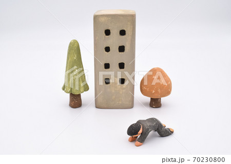 白背景に粘土で作られたミニチュアのビルと木々、落ち込む男性 白背景に粘土で作られたミニチュアのビルと木々、落ち込む男性 70230800