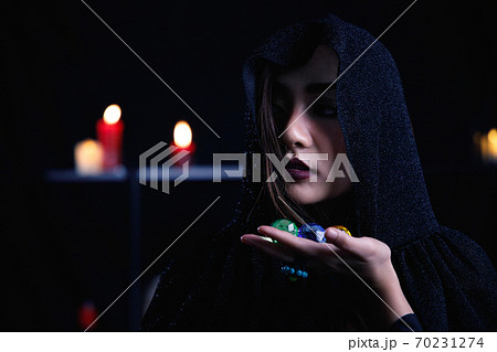 Mystery woman in black hood hold colorful gem on dark background. Mystery woman in black hood hold colorful gem on dark background. 70231274