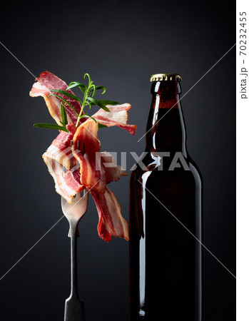 Unopened beer bottle and slices of fried bacon garnished with rosemary. Unopened beer bottle and slices of fried bacon garnished with rosemary. 70232455