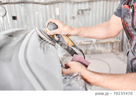 The mechanic works with a grinding tool. Sanding of car elements. Garage painting car service. Repairing car section after the accident. 70235470