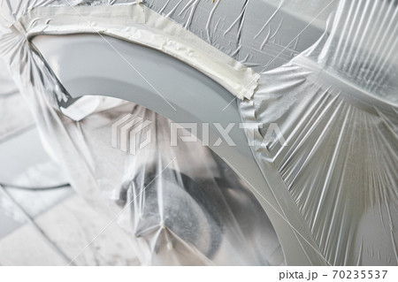 Garage painting car service. section of the car is covered with primer. vehicle is covered with protective paper. Repairing car body work after the accident by working sanding primer before painting. Garage painting car service. section of the car is covered with primer. vehicle is covered with protective paper. Repairing car body work after the accident by working sanding primer before painting. 70235537