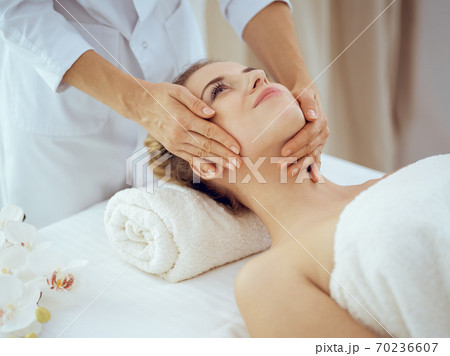Young and blonde woman enjoying facial massage in spa salon. Beauty concept Young and blonde woman enjoying facial massage in spa salon. Beauty concept 70236607
