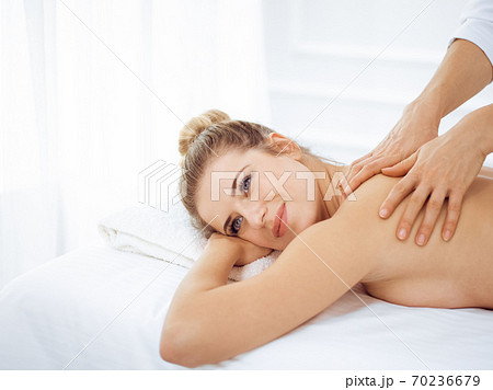 Young and blonde woman enjoying massage of back in spa salon. Beauty concept 70236679