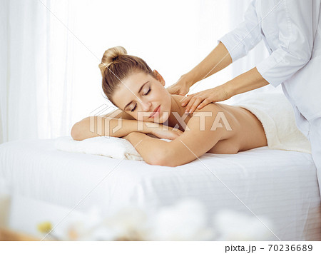 Young and blonde woman enjoying massage of back in spa salon. Beauty concept Young and blonde woman enjoying massage of back in spa salon. Beauty concept 70236689