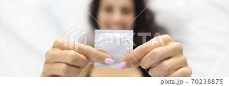 Woman holding condom while lying in bed. Woman holding condom while lying in bed. 70238875