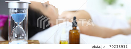Woman lies in spa salon next to an hourglass and aromatic oils 70238951