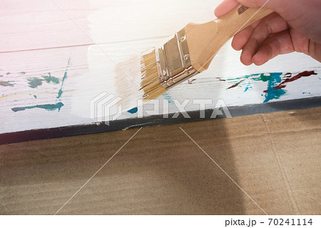 human hand holding brush painting white color on a white wooden table. human hand holding brush painting white color on a white wooden table. 70241114