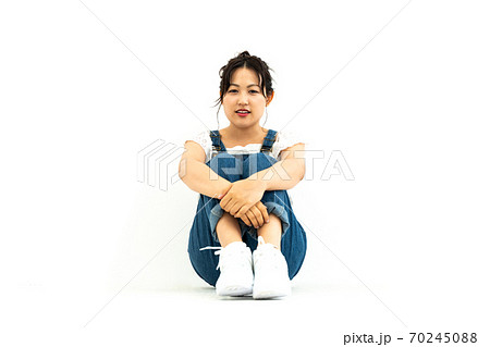膝を抱えるオーバーオールをはいた若い女性の写真素材