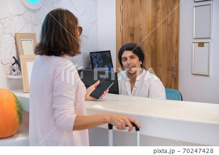 Portrait of female guest with suitcase, male hotel worker near reception Portrait of female guest with suitcase, male hotel worker near reception 70247428
