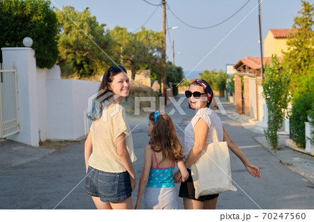 Mother and two daughters teenager and youngest walking together holding hands Mother and two daughters teenager and youngest walking together holding hands 70247560