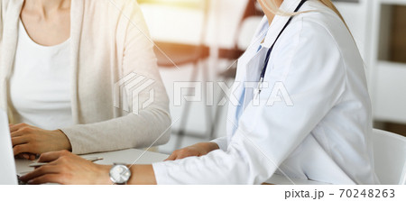 Unknown woman-doctor communicating with female patient in sunny clinic. Physician checks medical history record and exam results, close-up 70248263