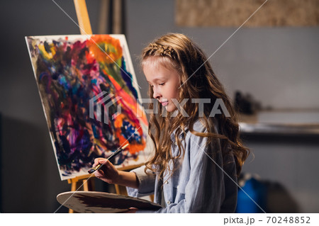 Abstract painting lesson. A little cute girl writes a color picture in oil or acrylic technique. Abstract painting lesson. A little cute girl writes a color picture in oil or acrylic technique. 70248852