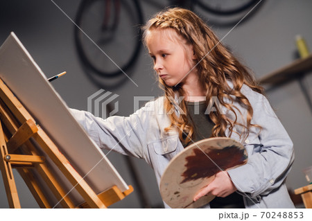 Young girl creative artist at work in a workshop. With passion draws a picture immersed in work. 70248853