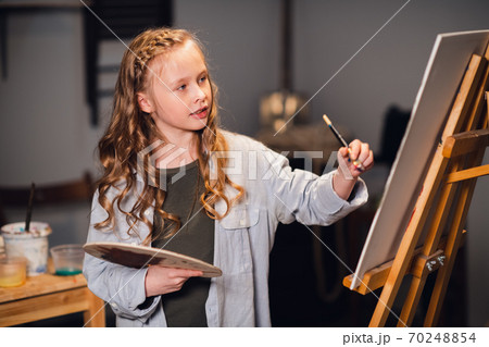 Young girl creative artist at work in a workshop. With passion draws a picture immersed in work. Young girl creative artist at work in a workshop. With passion draws a picture immersed in work. 70248854
