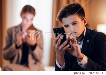 A kid texting messages on his smartphone, his older sister in th A kid texting messages on his smartphone, his older sister in th 70248891
