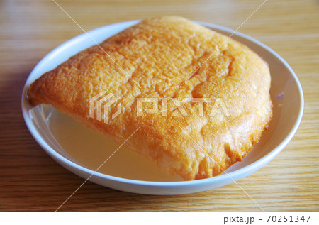 トーストした食パンの端を白い皿に載せて木目のテーブルに置いた状態の写真 70251347