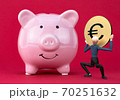 A caractere holding a euro golden coin in his hands in victory motion right next to a piggy bank 70251632