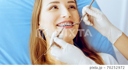 Smiling young woman with orthodontic brackets examined by dentist in dental clinic. Healthy teeth and medical care concept 70252972