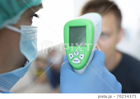 Doctor in a protective medical mask measures temperature of patient. 70254375