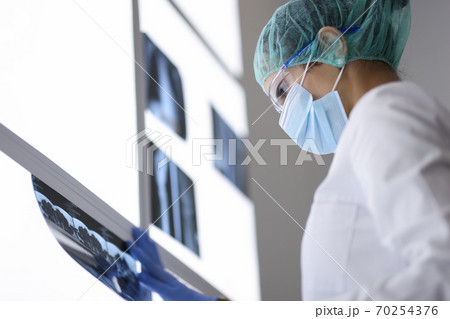 Doctor in protective medical mask and glasses looks at an X-ray. Doctor in protective medical mask and glasses looks at an X-ray. 70254376