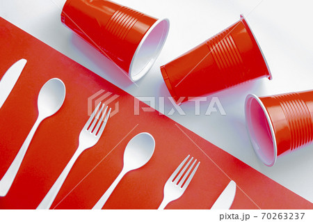Horizontal view of single use white plastic cutlery and red plastic glass on a red and white background. Concept Horizontal view of single use white plastic cutlery and red plastic glass on a red and white background. Concept 70263237