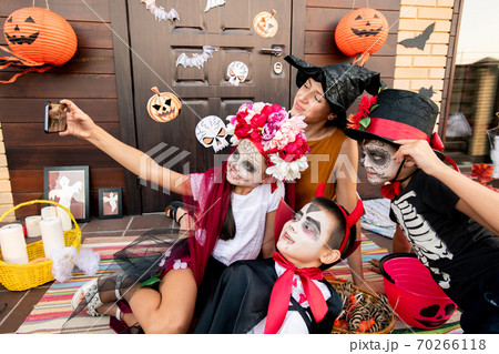 Cute halloween girl with smartphone making selfie with two boys and young woman Cute halloween girl with smartphone making selfie with two boys and young woman 70266118