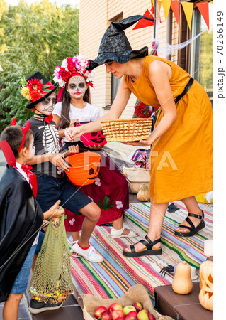 Young female in yellow dress and black witch hat bending in front of kids 70266149
