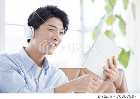 ヘッドフォンをしてタブレットを見る若い男性 ヘッドフォンをしてタブレットを見る若い男性 70267987