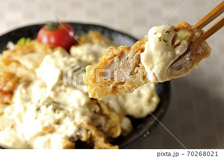 ミニトマトなど野菜も一緒に乗っているタルタルソースたっぷりのチキン南蛮丼の一切れを箸でつまんで食べる ミニトマトなど野菜も一緒に乗っているタルタルソースたっぷりのチキン南蛮丼の一切れを箸でつまんで食べる 70268021