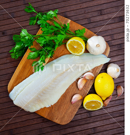 Raw cod fillet with garlic and lemon on wooden surface Raw cod fillet with garlic and lemon on wooden surface 70273632