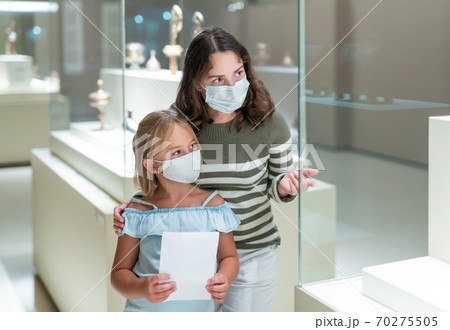 Woman visitor looking to art objects under glass with guide book 70275505