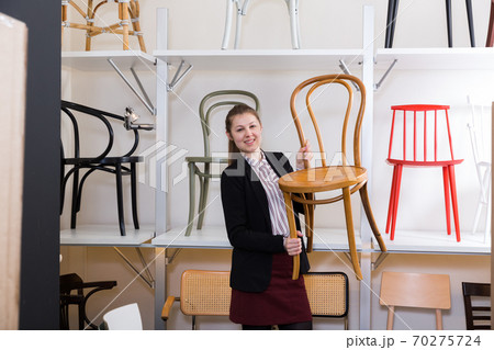 Saleswoman offering wooden chairs in store 70275724