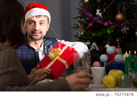 Man in hat giving present to woman at New Year dinner Man in hat giving present to woman at New Year dinner 70275878