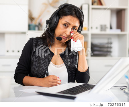 Upset woman wearing microphone headset at workplace in office 70276315
