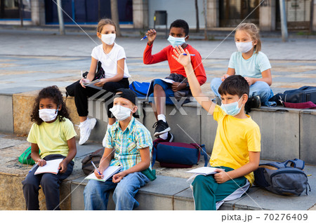 Preteen schoolchildren in protective masks with workbooks in schoolyard 70276409