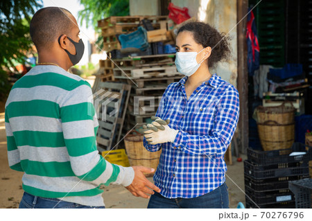 Male and female farmers in protective masks discussing outdoors Male and female farmers in protective masks discussing outdoors 70276796