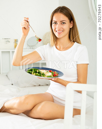 Cheerful young girl in lingerie having a salad while laying in the bed Cheerful young girl in lingerie having a salad while laying in the bed 70276943