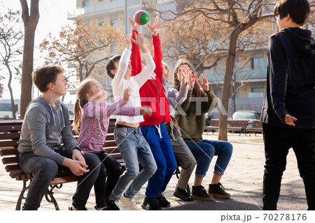 Group of cheerful children relaxing on bench on playground, playing with ball Group of cheerful children relaxing on bench on playground, playing with ball 70278176