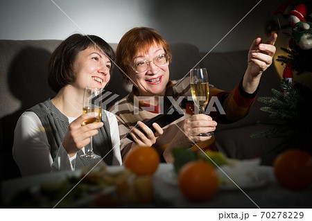 Happy mother and daughter drink champagne and watch TV on Christmas night 70278229