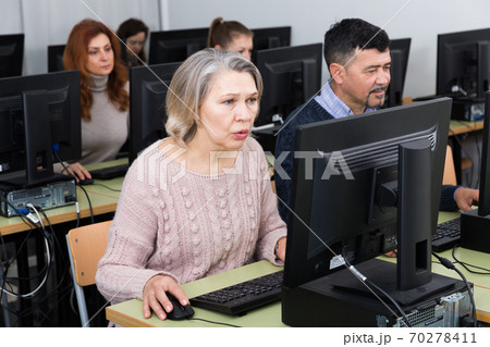 Young and older businesswomen and businessmen in open plan office 70278411