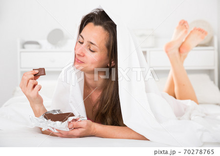 Woman in sleepwear relaxing and eating chocolate in bed in bedroom 70278765
