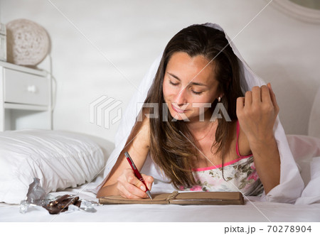 Woman elaxing under blanket and making schedule for tomorrow 70278904