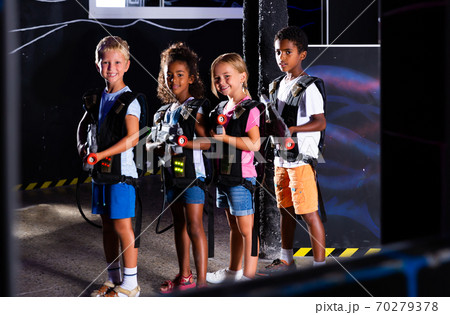 Group portrait of positive smiling teenagers with laser guns having fun on dark lasertag arena 70279378