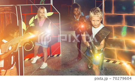 Joyful teens aiming laser guns at other players during lasertag game in dark room 70279604