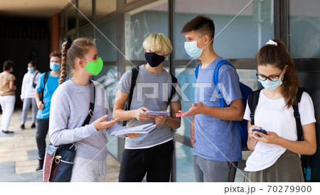 Group of students in protective masks discuss past lessons at a college on street Group of students in protective masks discuss past lessons at a college on street 70279900