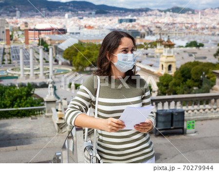 Traveling girl in protective mask looking at the guide in city european street Traveling girl in protective mask looking at the guide in city european street 70279944
