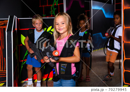 Smiling girl aiming laser gun at other players during lasertag game in dark room Smiling girl aiming laser gun at other players during lasertag game in dark room 70279945