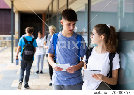 Two teenage students exchange lectures near the college building on summer day 70280353