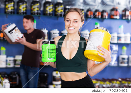 sporty woman holding big cans of sport nutrition 70280401